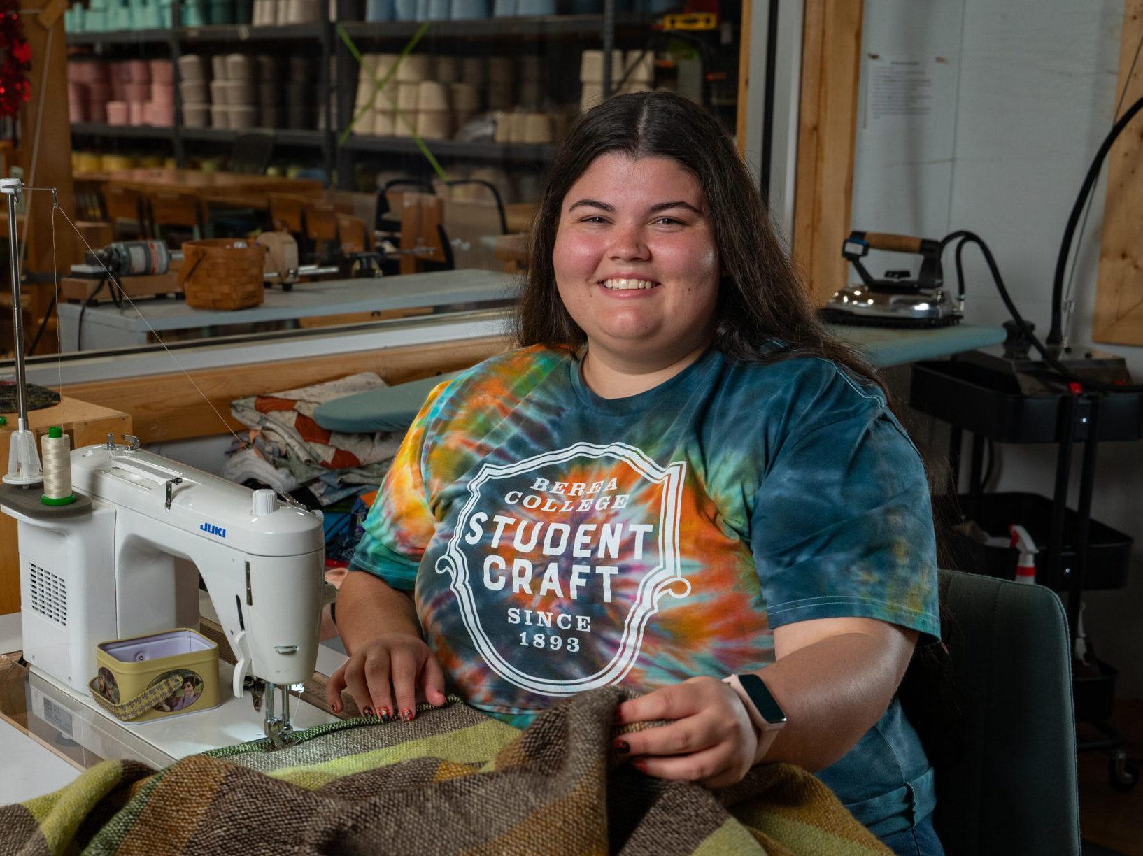 Berea student, Dani '25, smiling at the camera while holding a blanket that she's working on.